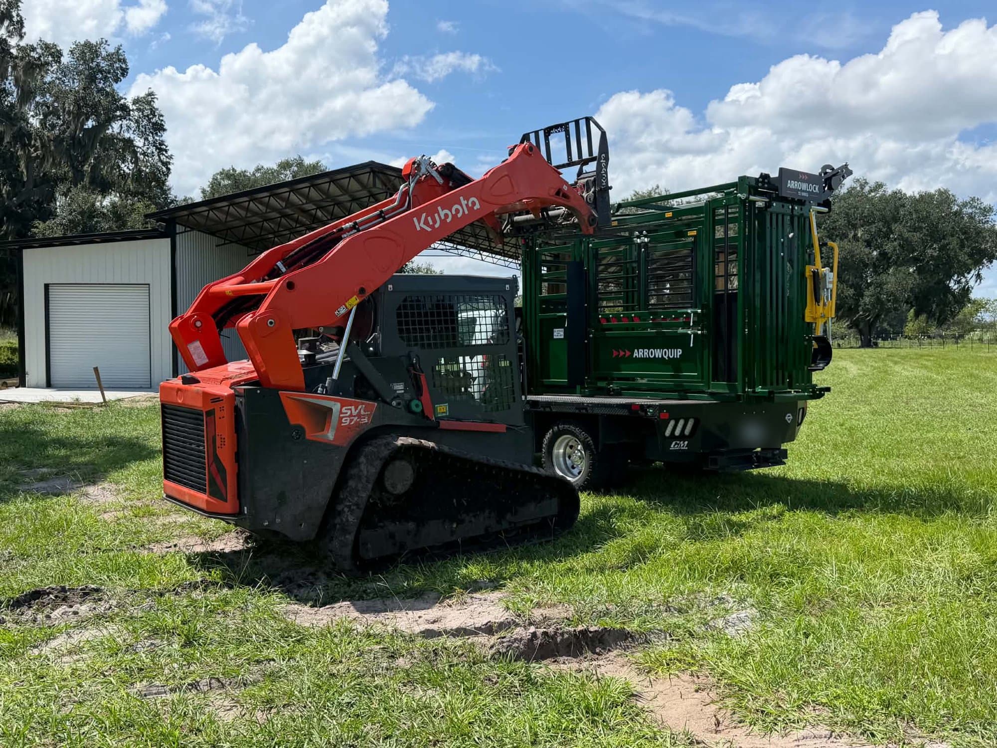 Kubota SVL75 de Javi's con horquillas levantando una manga ganadera Arrowquip de la plataforma del camión de un cliente junto a un establo
