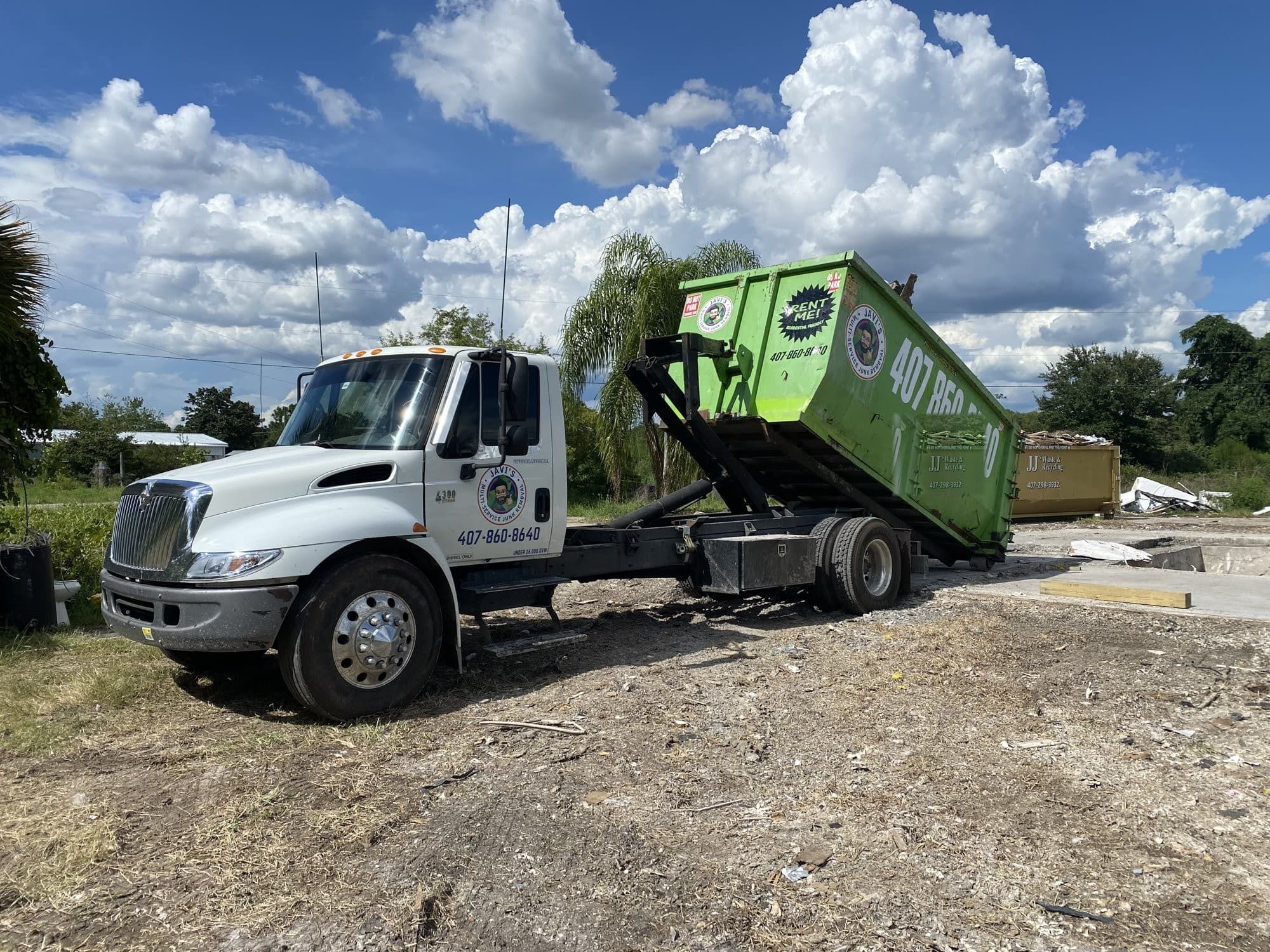 Camión de Javi's cargando un contenedor verde en una obra bajo el cielo de Florida