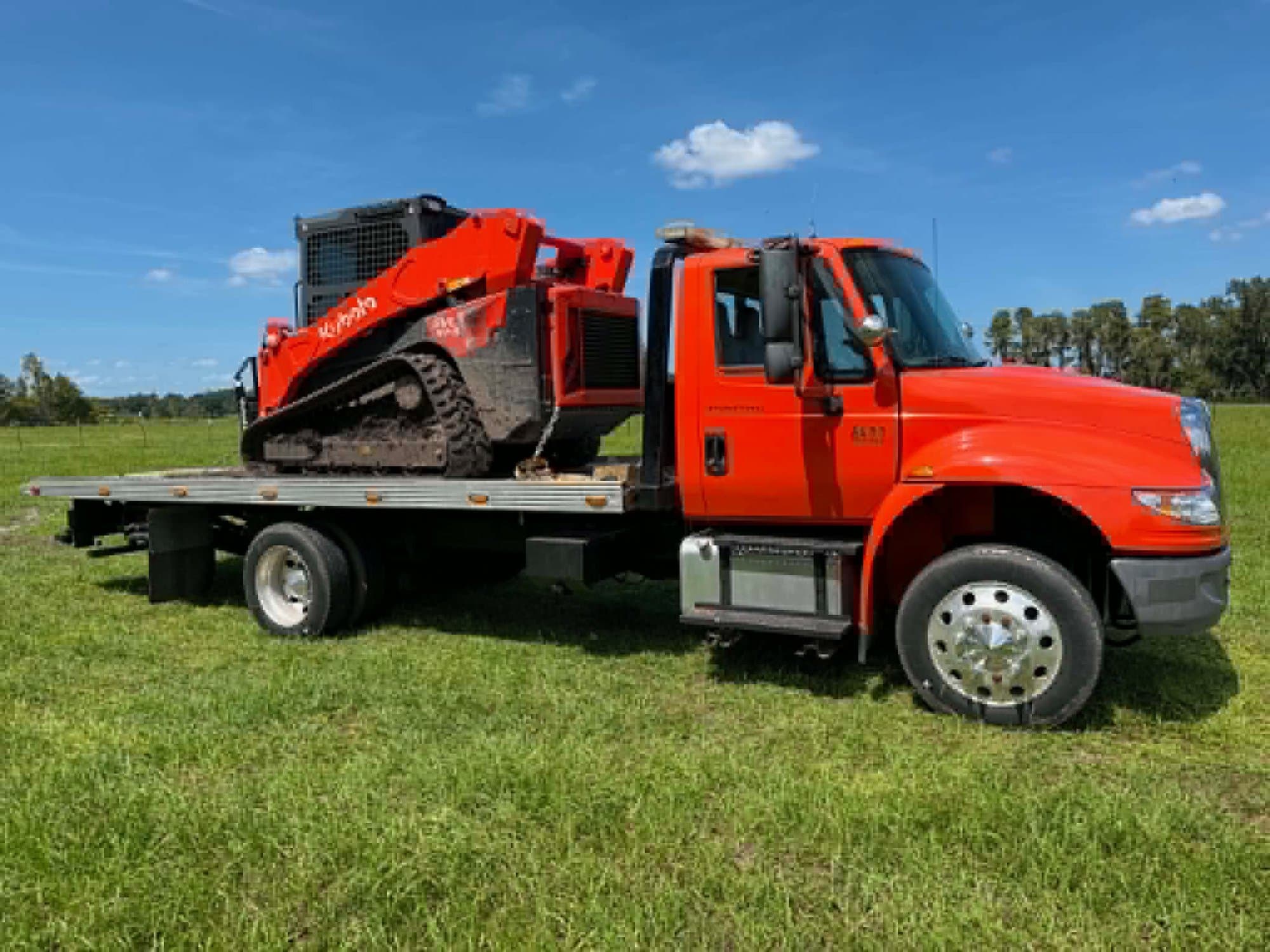 Plataforma de Javi's cargando un cargador compacto de orugas Kubota a través de un campo